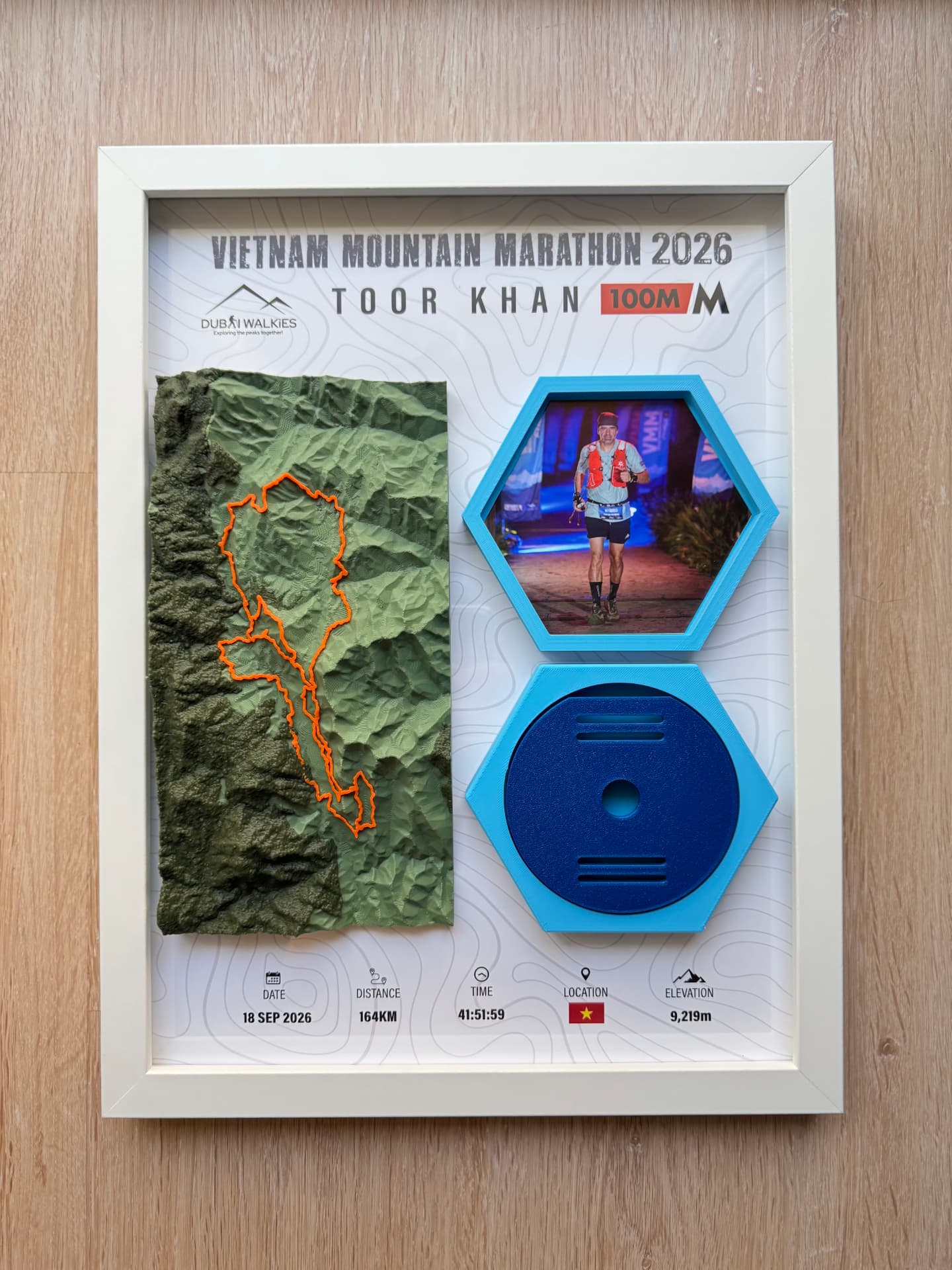 Vietnam Mountain Marathon 2026 — Full Frame — Green hex relief with the orange route line, finisher photo and medal mount in one display.